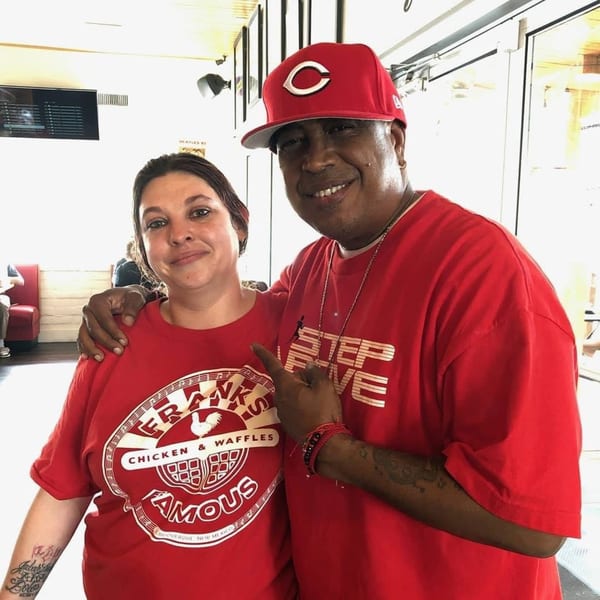Two smiling people in red Frank's Famous Chicken & Waffles shirts pose together indoors.