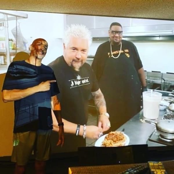 Guy Fieri and two men in a kitchen, with Fieri preparing a plate of Frank's Famous chicken and waffles.