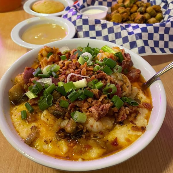 A bowl of Frank's Famous shrimp and grits, topped with bacon and green onions, with sides.