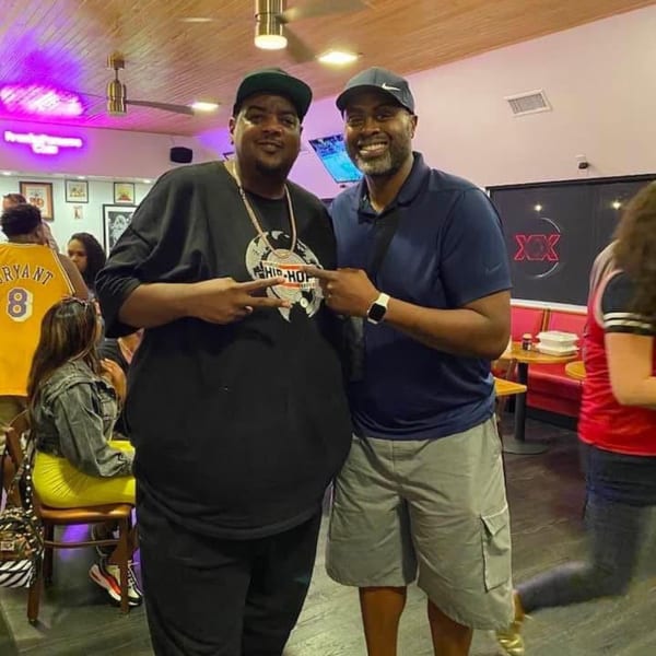 Two men smiling and posing for a photo inside Frank's Famous Chicken & Waffles restaurant.