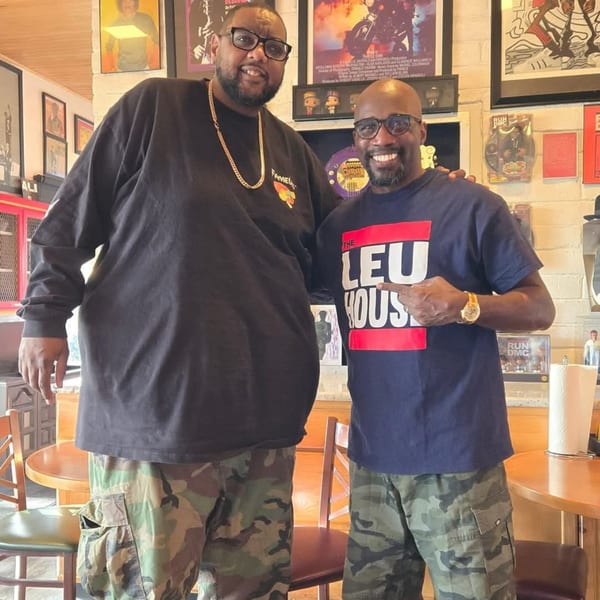Two men in camouflage pants and t-shirts smiling, standing in Frank's Famous Chicken & Waffles.