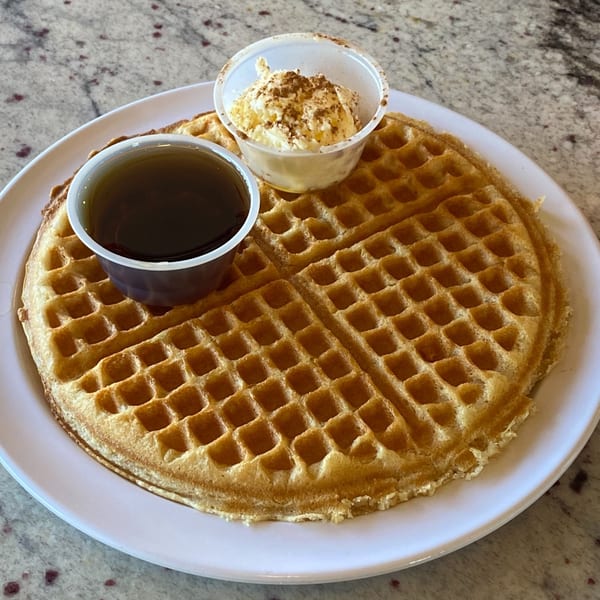 Golden waffle on a white plate with syrup and cinnamon butter in small cups.