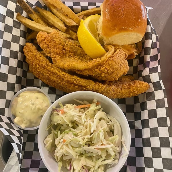 Frank's Famous fried catfish, fries, a roll, coleslaw, and tartar sauce in a checkered basket.