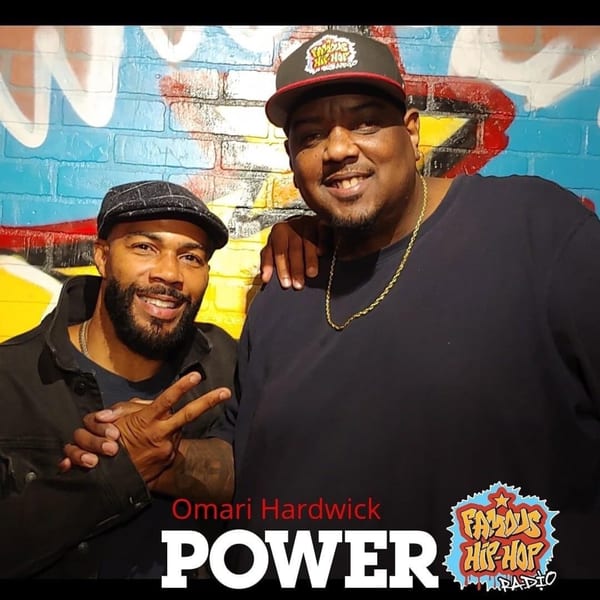 Two men, Omari Hardwick and another, smiling in front of a colorful graffiti wall at Frank's Famous.