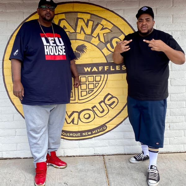 Two men posing in front of a Frank's Famous Chicken & Waffles mural.