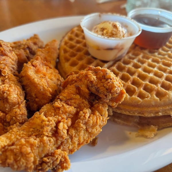 Crispy fried chicken tenders and golden waffles with butter and syrup on a white plate.