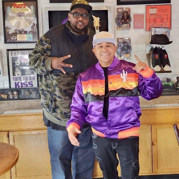 Two men posing in Frank's Famous Chicken & Waffles, surrounded by music memorabilia.