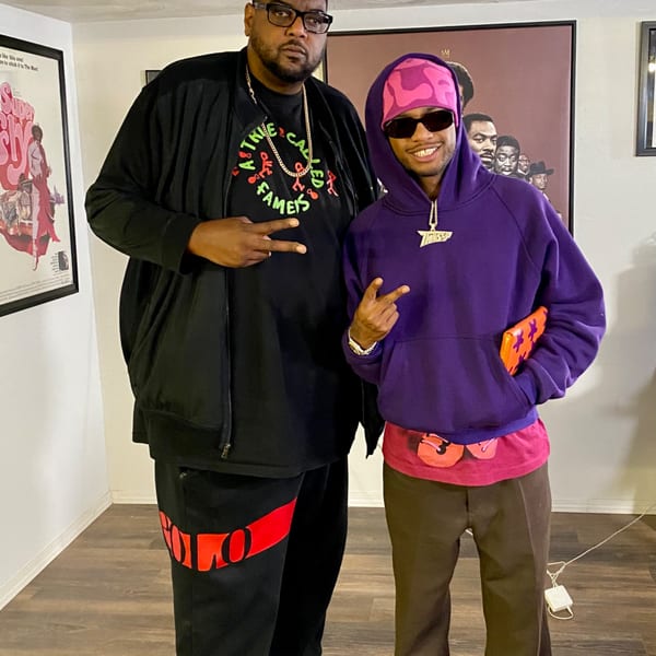 Two men posing for a photo, one in a black shirt and the other in a purple hoodie.