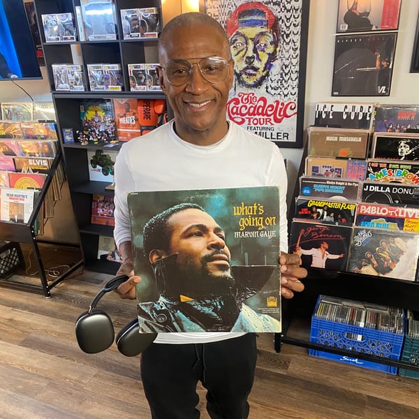 Man in glasses holding a Marvin Gaye "What's Going On" record album in a music store.