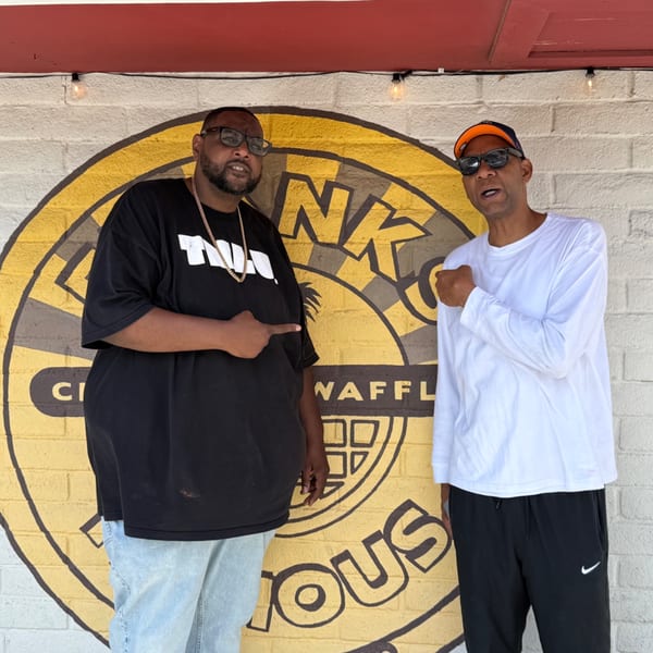 Two men posing in front of a Frank's Famous Chicken & Waffles mural.