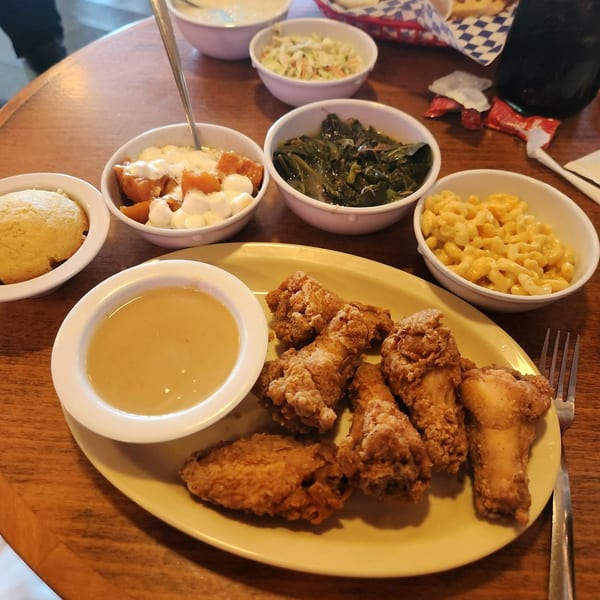 Frank's Famous Chicken & Waffles meal with fried chicken, gravy, mac and cheese, collard greens, sweet potatoes, and cornbread.