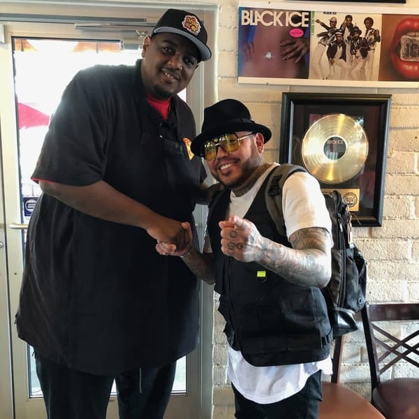 Two men shaking hands inside Frank's Famous Chicken & Waffles, with music memorabilia on the wall.